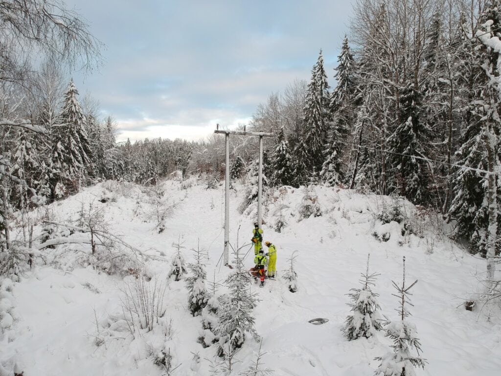 Three workers are seen in the forest in the snow repairing a telegraph pole.