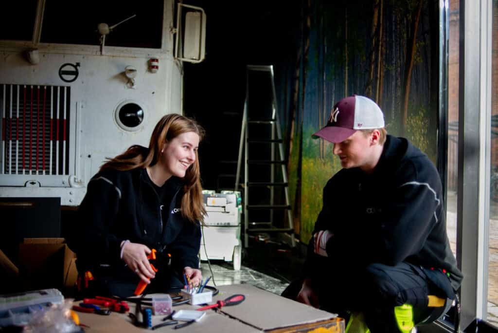 An apprentice receives input from a colleague as she completes some electric work.