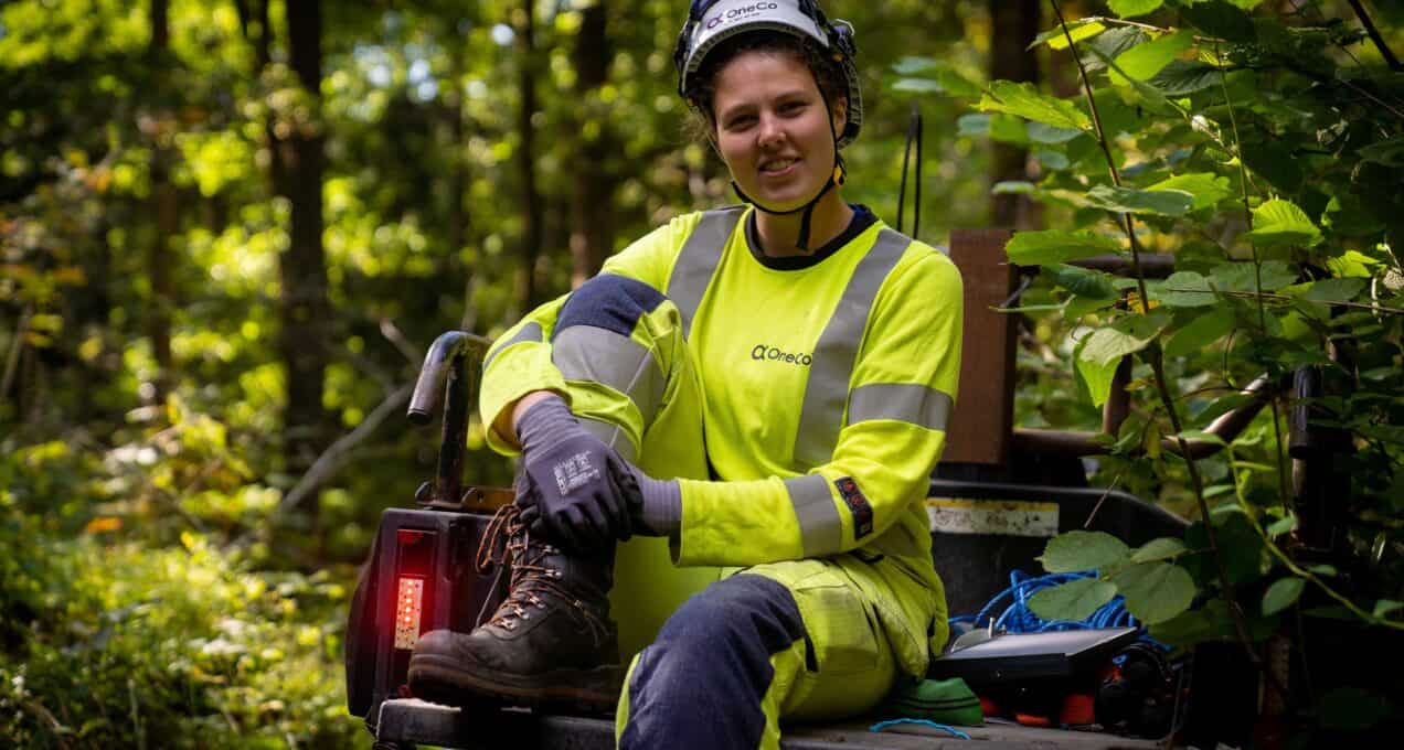 A OneCo worker is sitting in the back of a 4WD motorbike smiling at the camera.