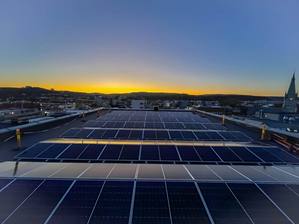 Solar panels installed on a roof are reflecting the golden sunset that is seen in the background.