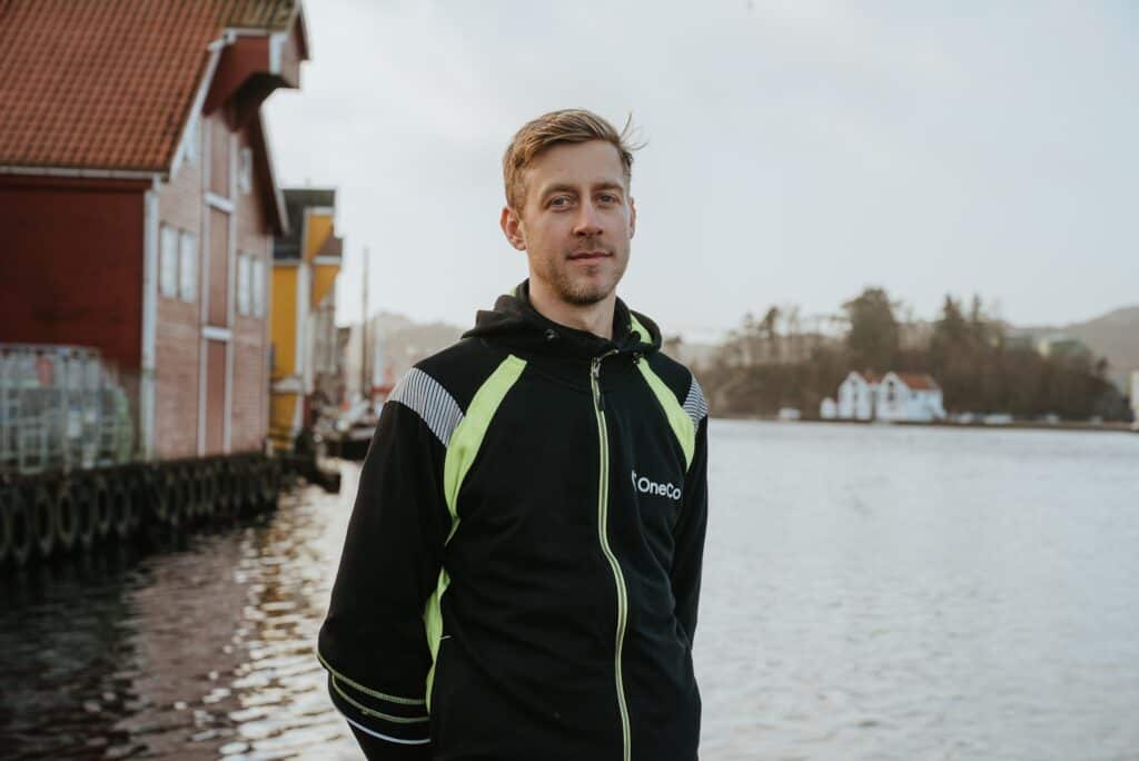 A OneCo worker is seen looking directly into the camera. The ocean is visible in the background.