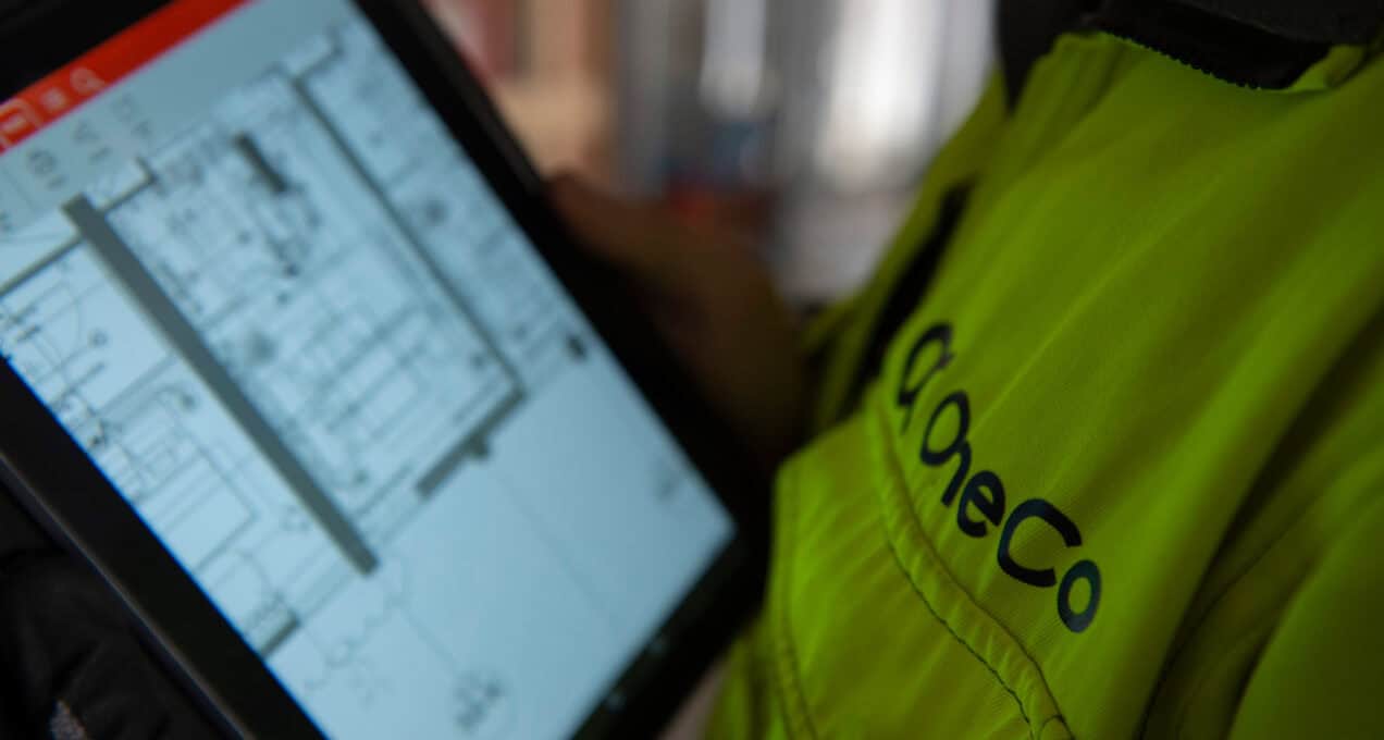 A closeup of a OneCo worker looking at an ipad. A technical drawing is visible on the screen.