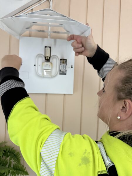 Bilde av en elektriker i OneCo som bytter ut gamle armaturer, med nye LED-armaturer